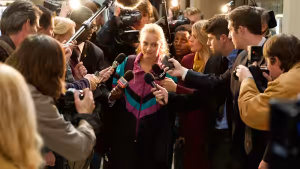 Tonya (Margot Robbie) faces a press scrum as reporters thrust microphones toward her