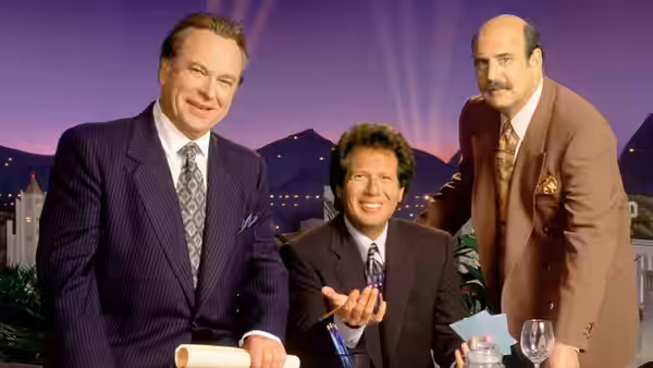 Larry Sanders (Garry Shandling) gesturing while seated with two suited men