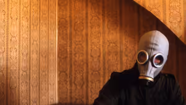 A person wearing a gas mask stands in front of patterned wooden wall
