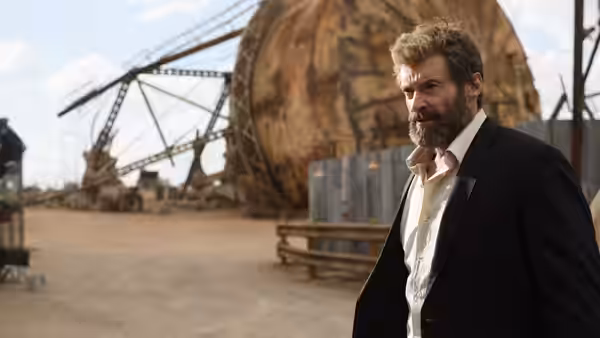 Logan (Hugh Jackman) standing in an industrial yard wearing a black suit