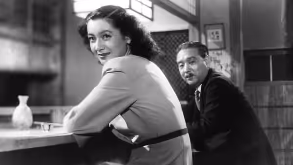 woman in light jacket leans on counter smiling over her shoulder while man watches