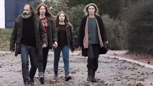 Four adults walking together on a path covered with fallen leaves