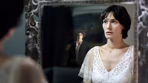 Woman in white lace dress with man reflected in ornate mirror