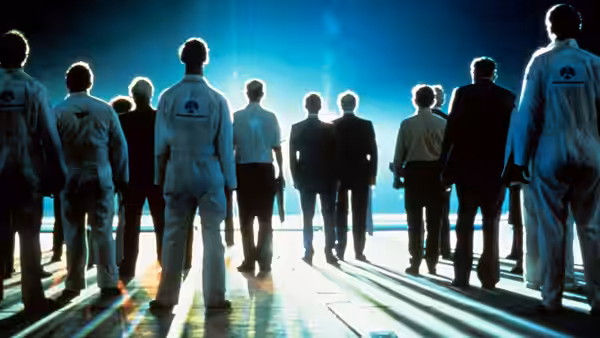 Group of men in jumpsuits facing a bright light on a runway