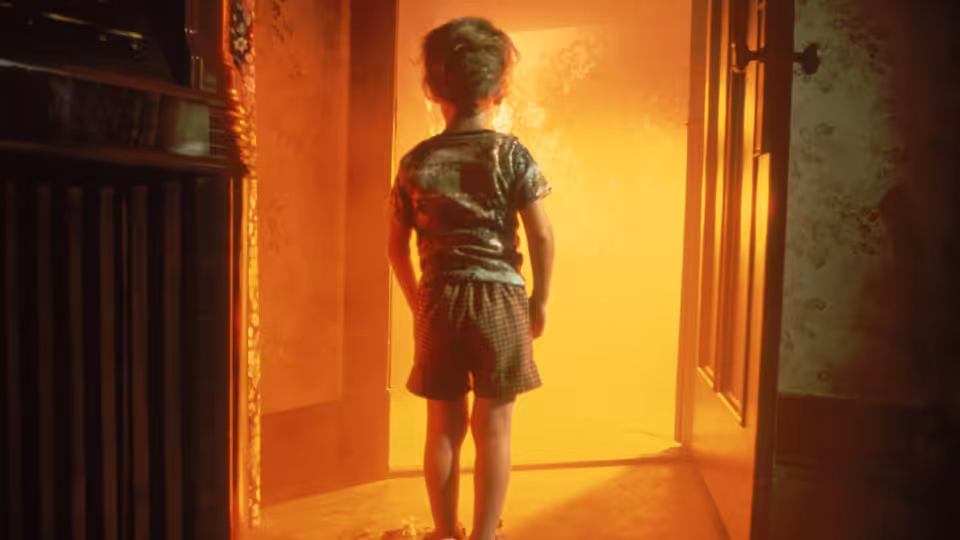 A young boy standing in a doorway facing a bright orange glow
