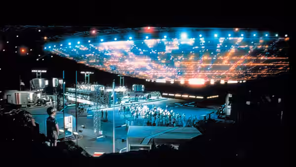 A massive glowing spacecraft hovering above an airfield at night