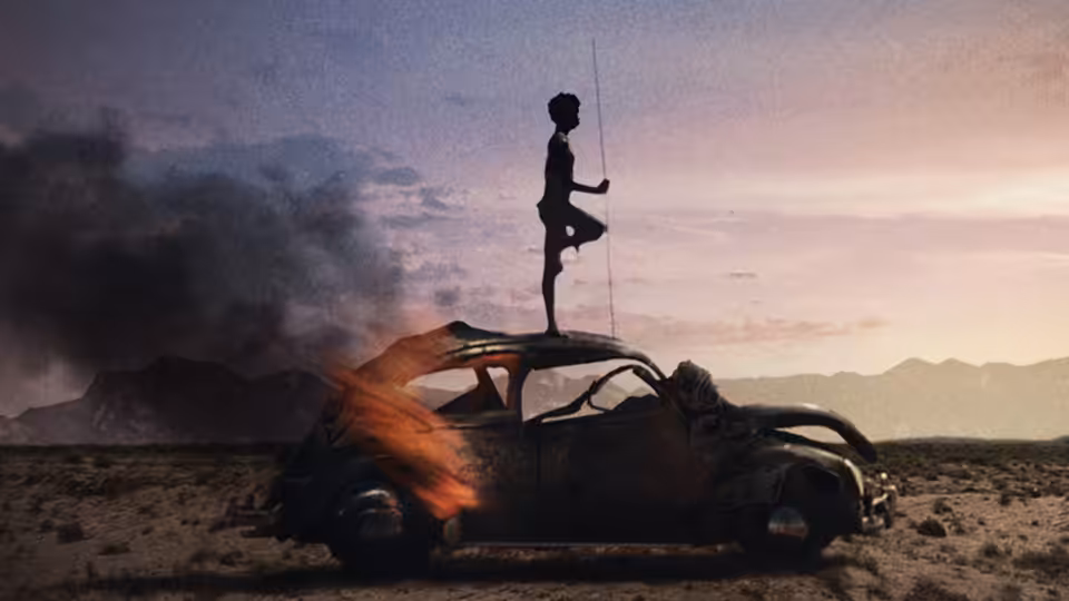 a figure standing on the roof of a burning car in the desert