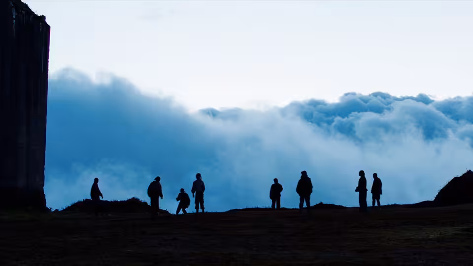 group of silhouetted figures standing on a ridge above the clouds