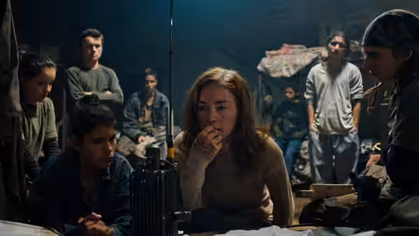 Doctora (Julianne Nicholson) with hand to mouth among a group in a room