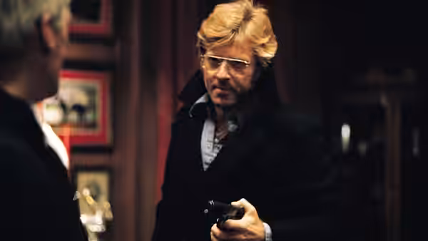 Joseph Turner (Robert Redford) holding a gun while facing another man indoors