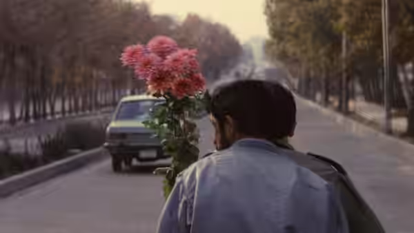 Man carrying pink flowers walking behind a car on a tree lined road