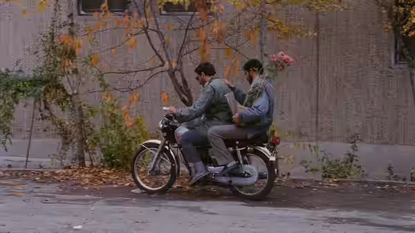 Two men riding a motorcycle with one holding pink flowers