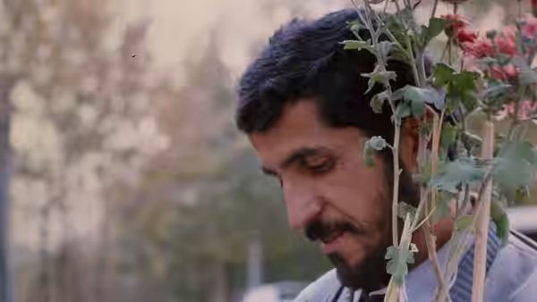Hossain Sabzian gazing downward beside a plant with pink flowers