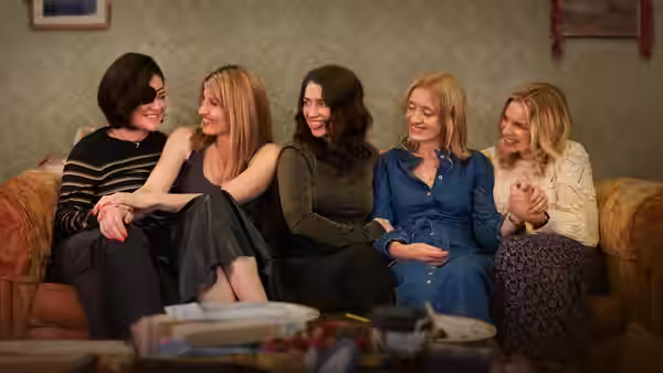 five women sitting together on a couch smiling and laughing