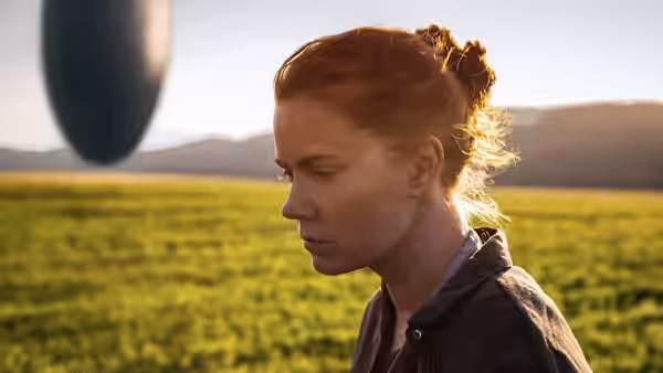 Louise Banks (Amy Adams) stands in a field gazing at a hovering craft