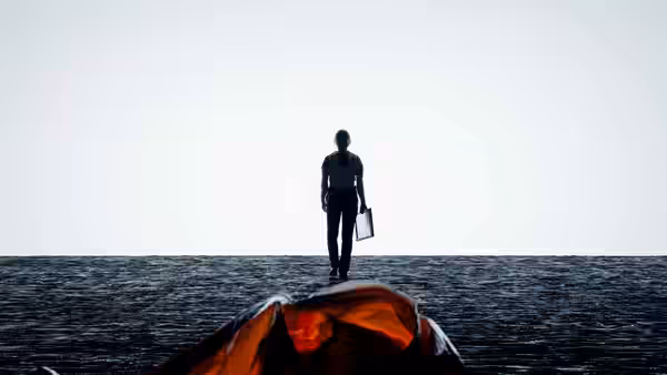 A silhouetted figure stands on dark ground holding a case beside orange fabric