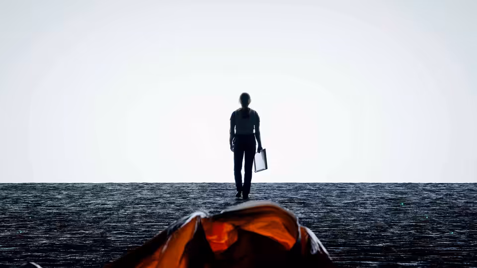 A silhouetted figure stands on dark ground holding a case beside orange fabric