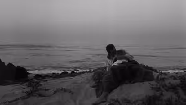 A couple sits together on a rocky beach facing the ocean
