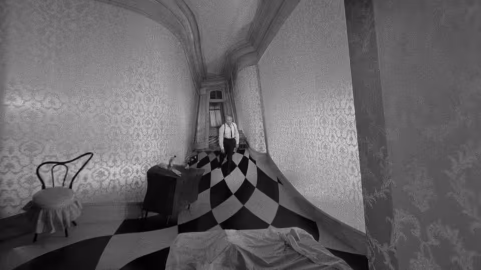 A man stands at the far end of a long, checkerboard-floored hallway