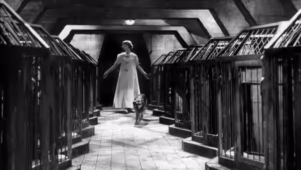 A woman in a white gown stands in a tiled corridor as a small dog waits nearby
