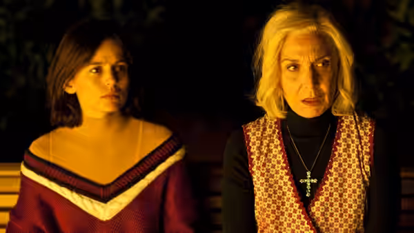 A young woman and an older woman stand together in the dark
