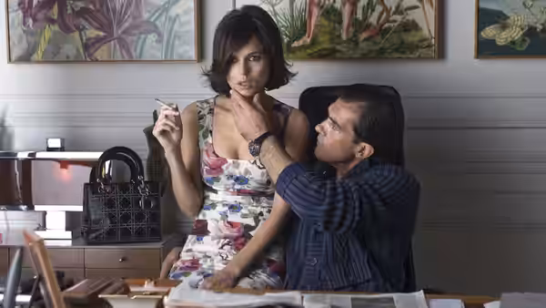 A seated man touches a young woman's chin as she holds a cigarette