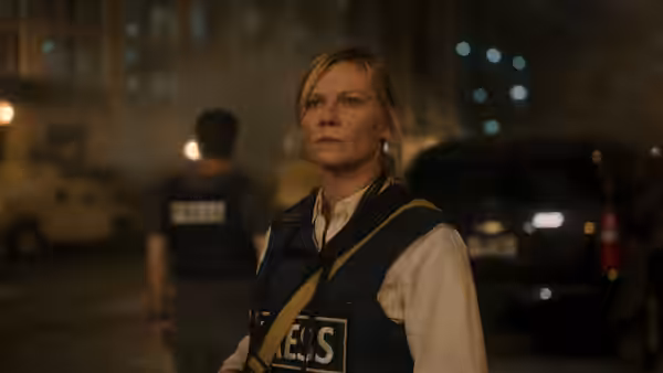 Lee (Kirsten Dunst) standing at night in a city street wearing a press vest