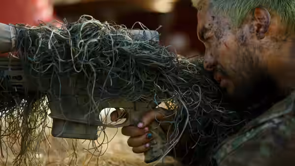 A dirt-covered soldier with green hair aiming a camouflaged rifle