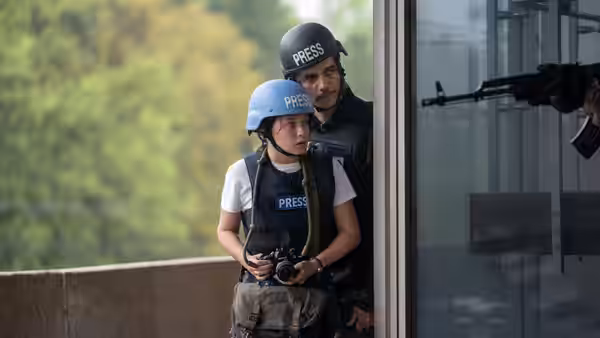 Jessie (Cailee Spaeny) and Joel (Wagner Moura) in press vests peering from a window