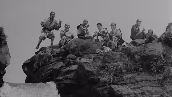 Men seated on rocky cliff with one standing and gesturing widely