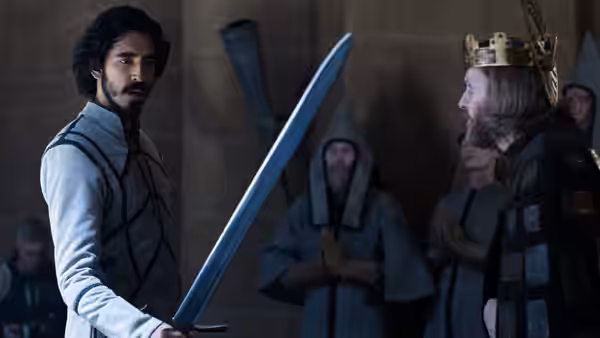 Gawain (Dev Patel) faces the crowned King (Sean Harris) with a sword in the hall