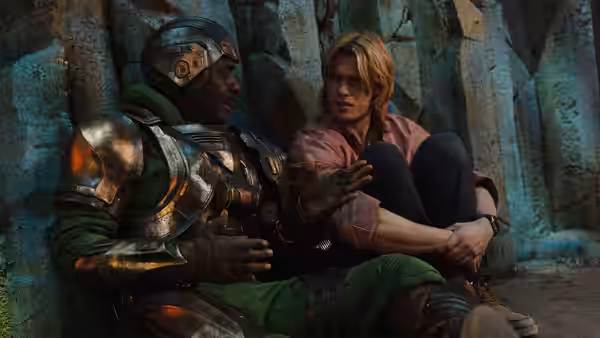 Adam (Nicholas Galitzine) sits bound beside armored Duncan (Idris Elba) in cave
