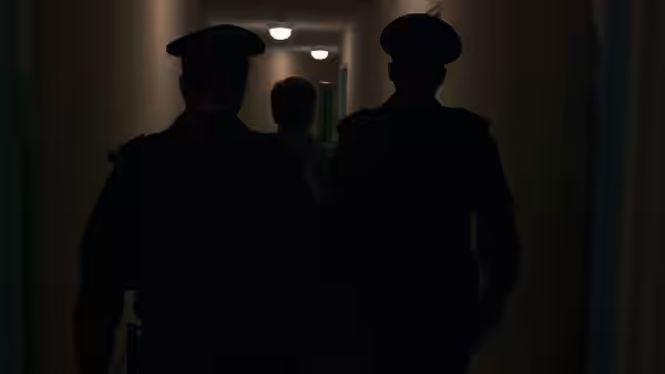 Two police officers walking behind boy down apartment hallway