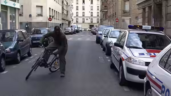 Man on bicycle riding past parked police cars on city street