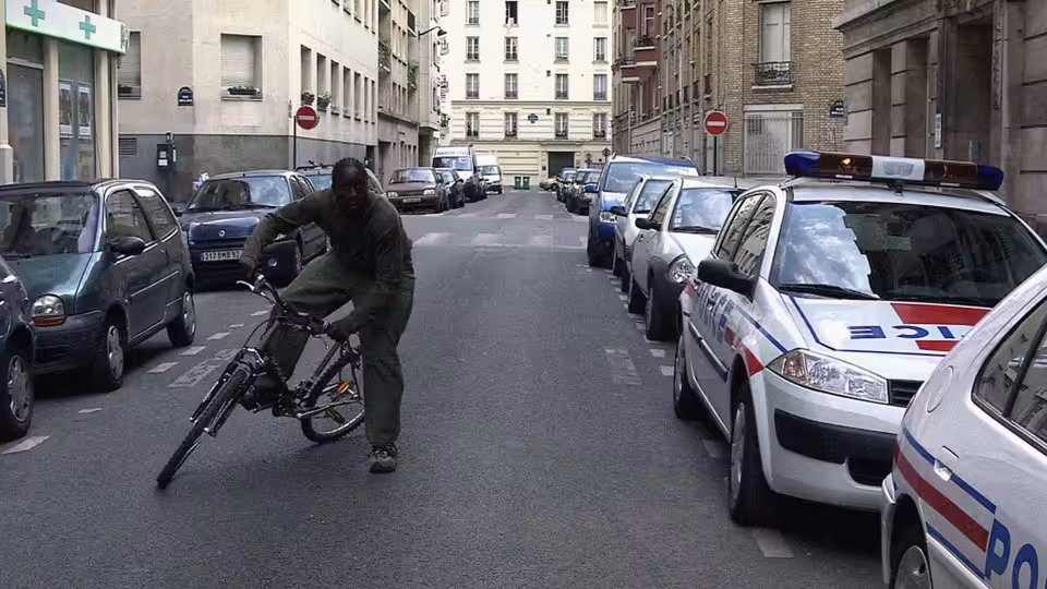 Man on bicycle riding past parked police cars on city street