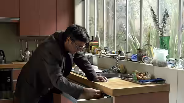 Man with glasses leaning over kitchen counter reaching into drawer