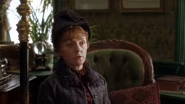 Lucy Gilbert (Lesley Manville) sits in an armchair wearing a hat and plaid coat