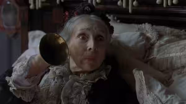 Elderly woman lies in bed holding an ear trumpet to her ear