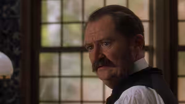 W. S. Gilbert (Jim Broadbent) looks back over his shoulder with a serious expression