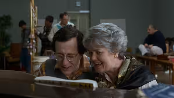 a man and woman with gray hair looking at sheet music at a piano