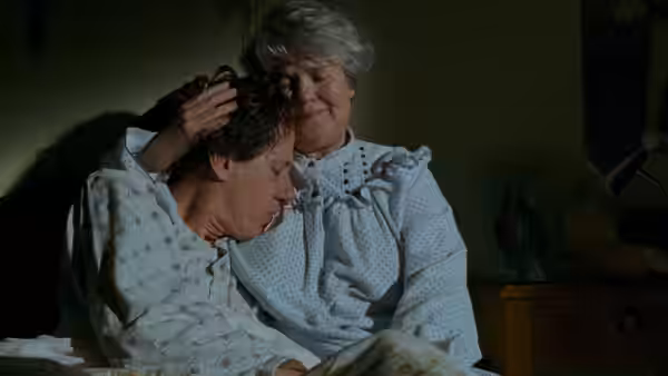 a woman with gray hair comforting a man lying in bed