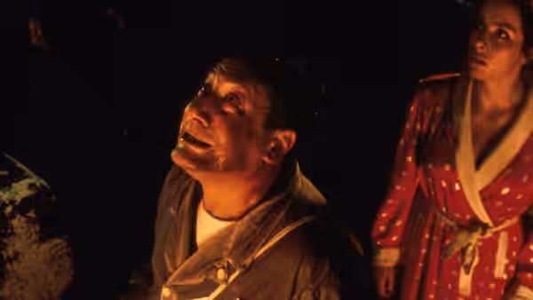 bloodied man looking up while standing beside a woman in a robe