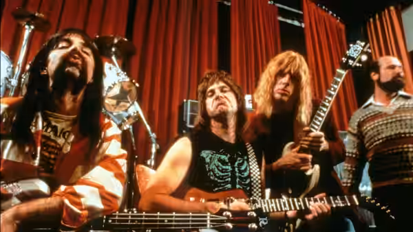 Three musicians play bass and guitars on a stage with red curtains