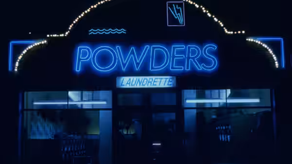 Blue neon POWDERS sign above the laundrette entrance at night
