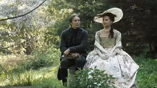 Johann Friedrich Struensee (Mads Mikkelsen) sits beside Caroline Mathilde (Alicia Vikander) in a garden