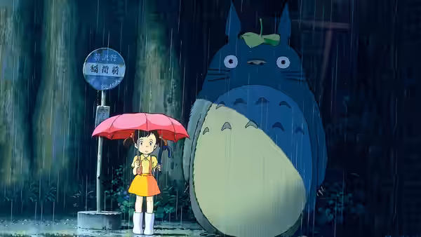 Satsuki holding a red umbrella beside Totoro at a rainy bus stop