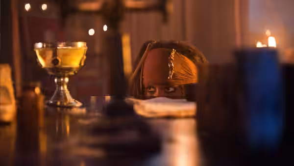 Jack Sparrow (Johnny Depp) peering over a table in a candlelit room