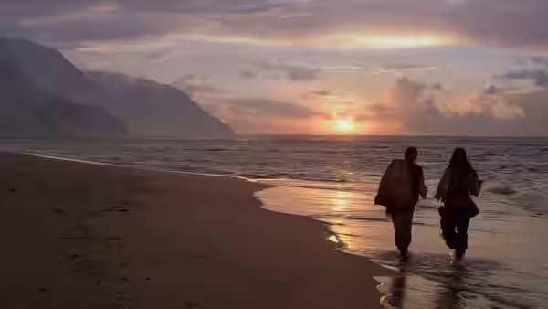 Two figures walking along a beach at sunset with mountains in the distance