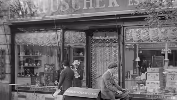 A man and a woman stand outside a decorated shop window as another man tends the storefront