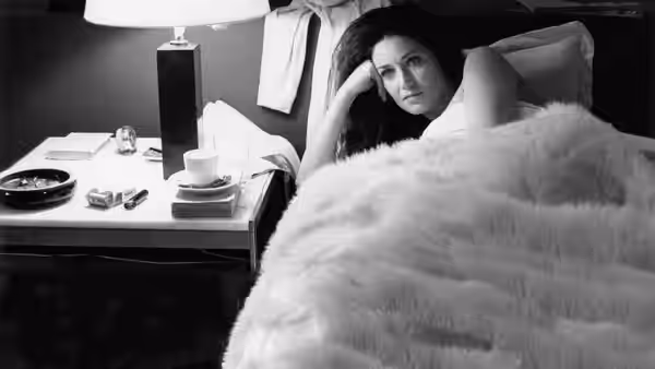 A woman reclines in bed beside a cluttered bedside table